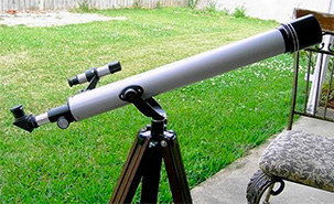 A small telescope on a tripod set up in a fenced backyard.