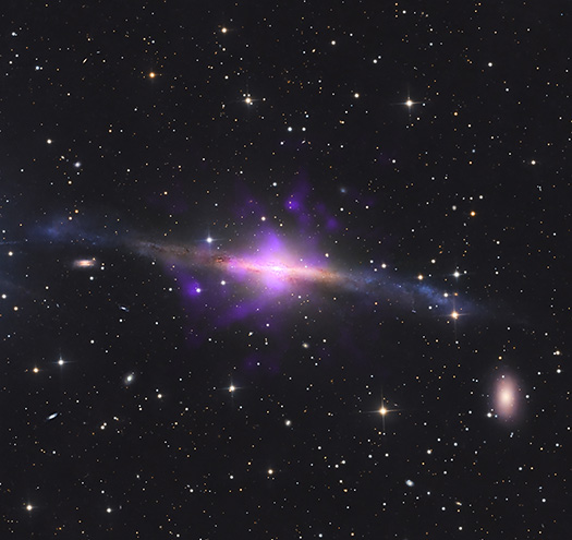 Image showing the structure of galaxy NGC 5084, with data from the Chandra X-ray Observatory overlaid on a visible-light image of the galaxy. Chandra’s data, shown in purple, revealed four plumes of hot gas emanating from a supermassive black hole rotating “tipped over” at the galaxy’s core.